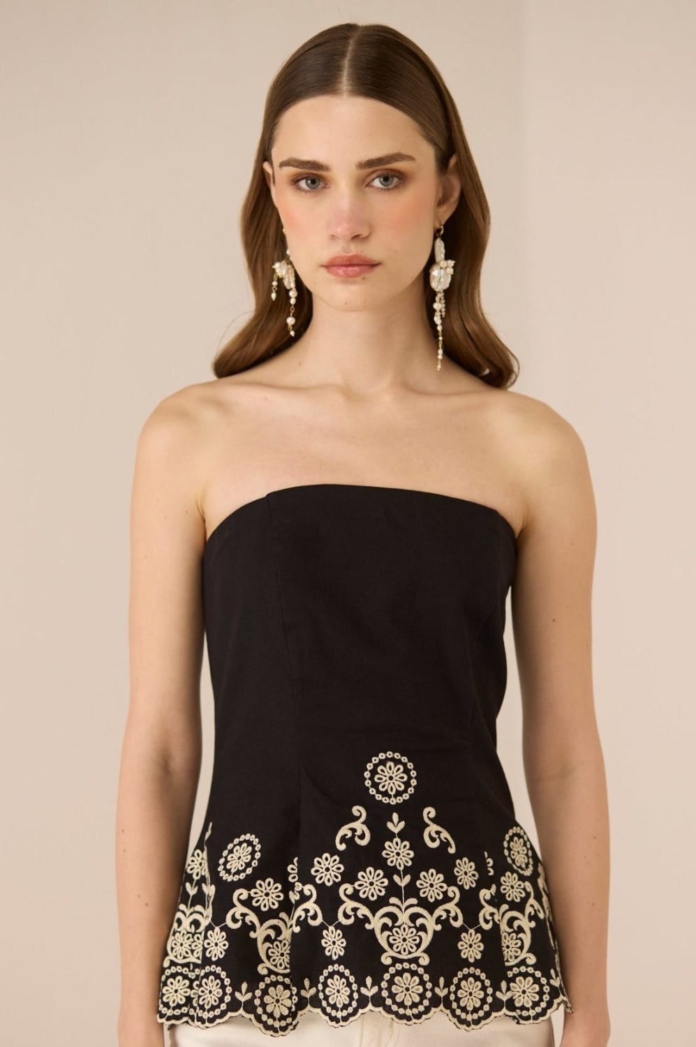 Woman wearing a black strapless top with white embroidery on a beige background Calling June