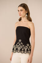 Woman wearing a black strapless top with white lace details on a beige background Calling June