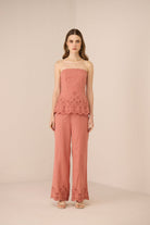 Woman wearing a pink strapless top and pants with lace details on a beige background Calling June