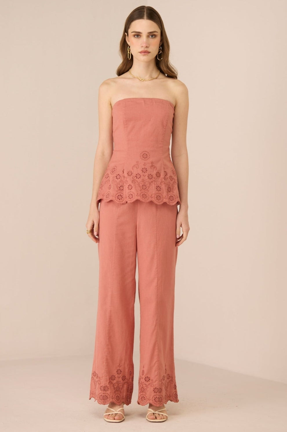 Woman wearing a pink strapless top and pants with lace details on a beige background Calling June