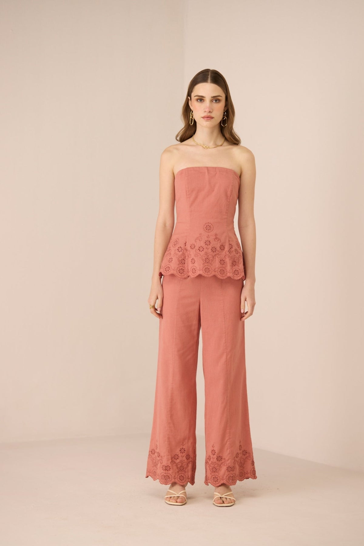 Woman wearing a coral strapless top and wide-leg pants with lace details on a beige background Calling June
