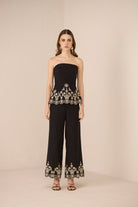 Woman wearing a black strapless top and wide-leg pants with embroidery on a beige background Calling June