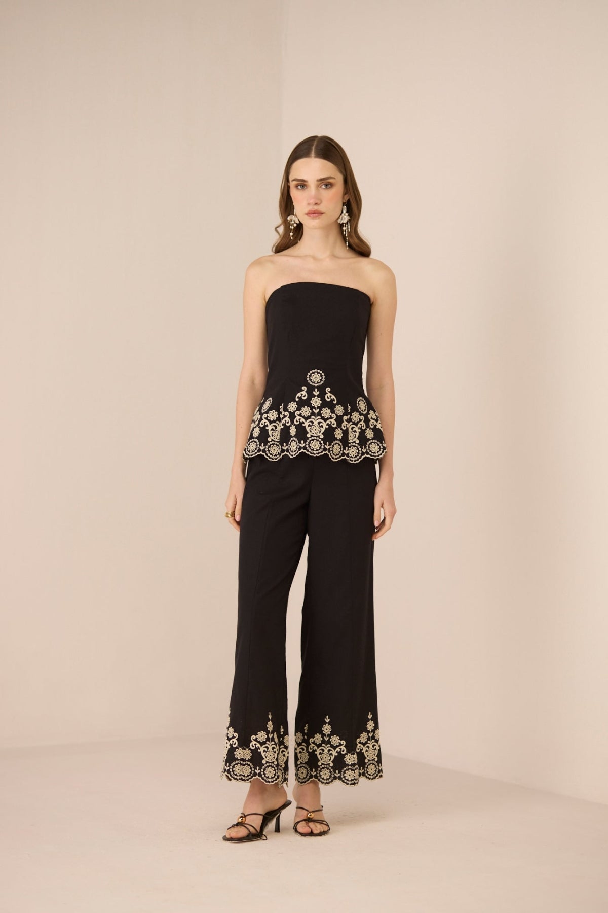 Woman wearing a black strapless top and pants with embroidery on a beige background Calling June
