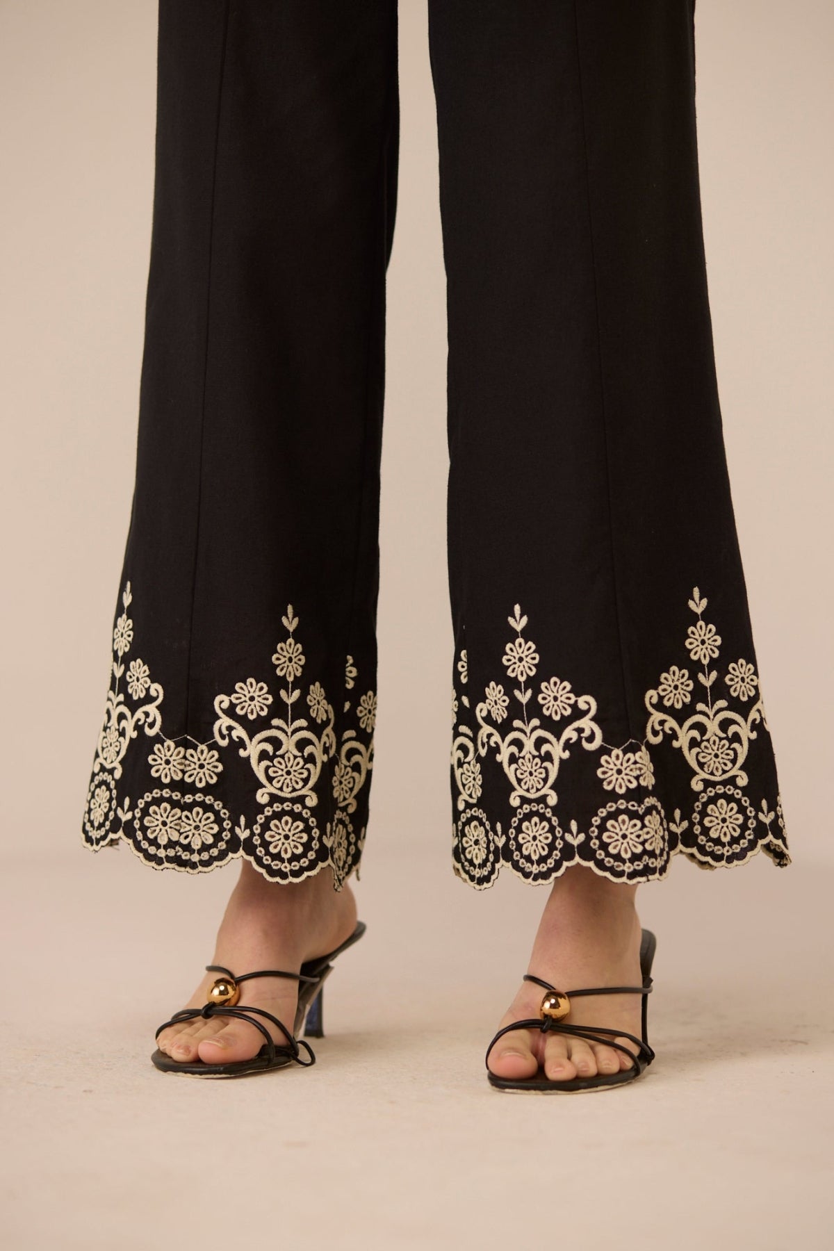 Black pants with white floral embroidery worn by a person on a beige background Calling June