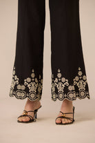 Black pants with white floral embroidery worn by a person on a beige background Calling June