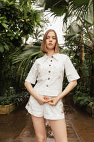 Woman in a white outfit standing in a lush, green outdoor setting Calling June