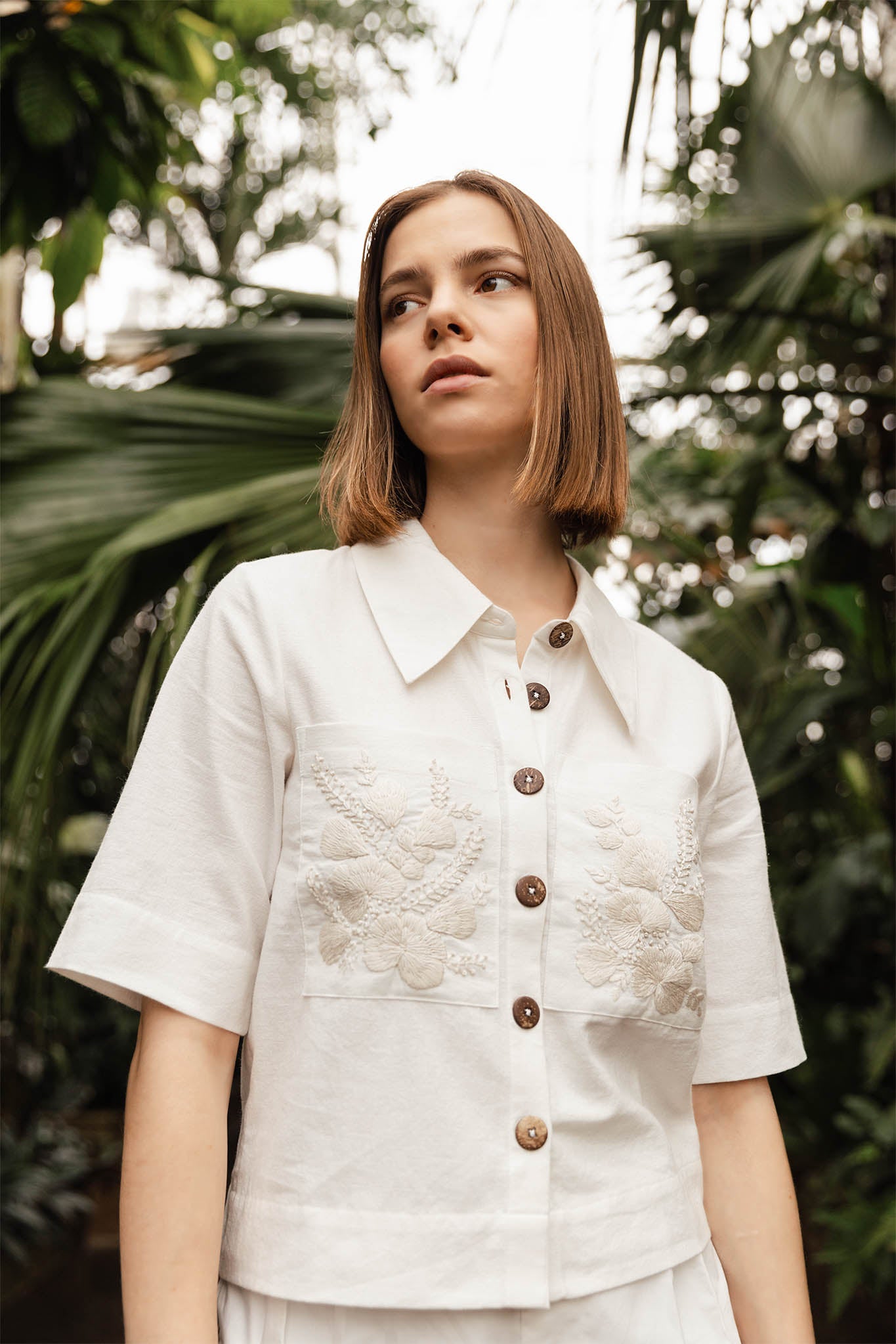 Woman wearing a white blouse with lace details and brown buttons against a blurred natural background Calling June