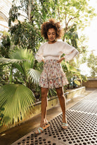 Woman in a floral dress standing in a lush, green indoor garden Calling June