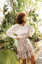Woman standing in a lush, green outdoor setting with plants and trees Calling June