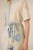 Person wearing a light-colored shirt with a floral pattern and a matching skirt on a neutral background Calling June