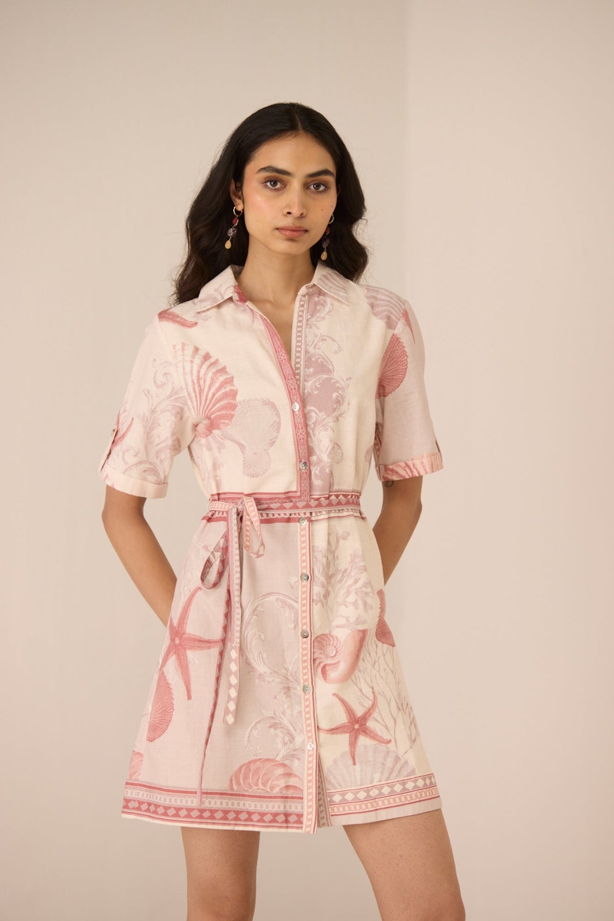 Woman wearing a pink and white dress with shell pattern on a beige background Calling June