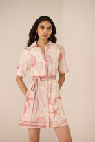 Woman wearing a pink and white dress with shell pattern on a beige background Calling June