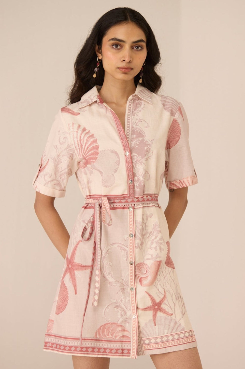 Woman wearing a pink and white dress with shell pattern on a beige background Calling June