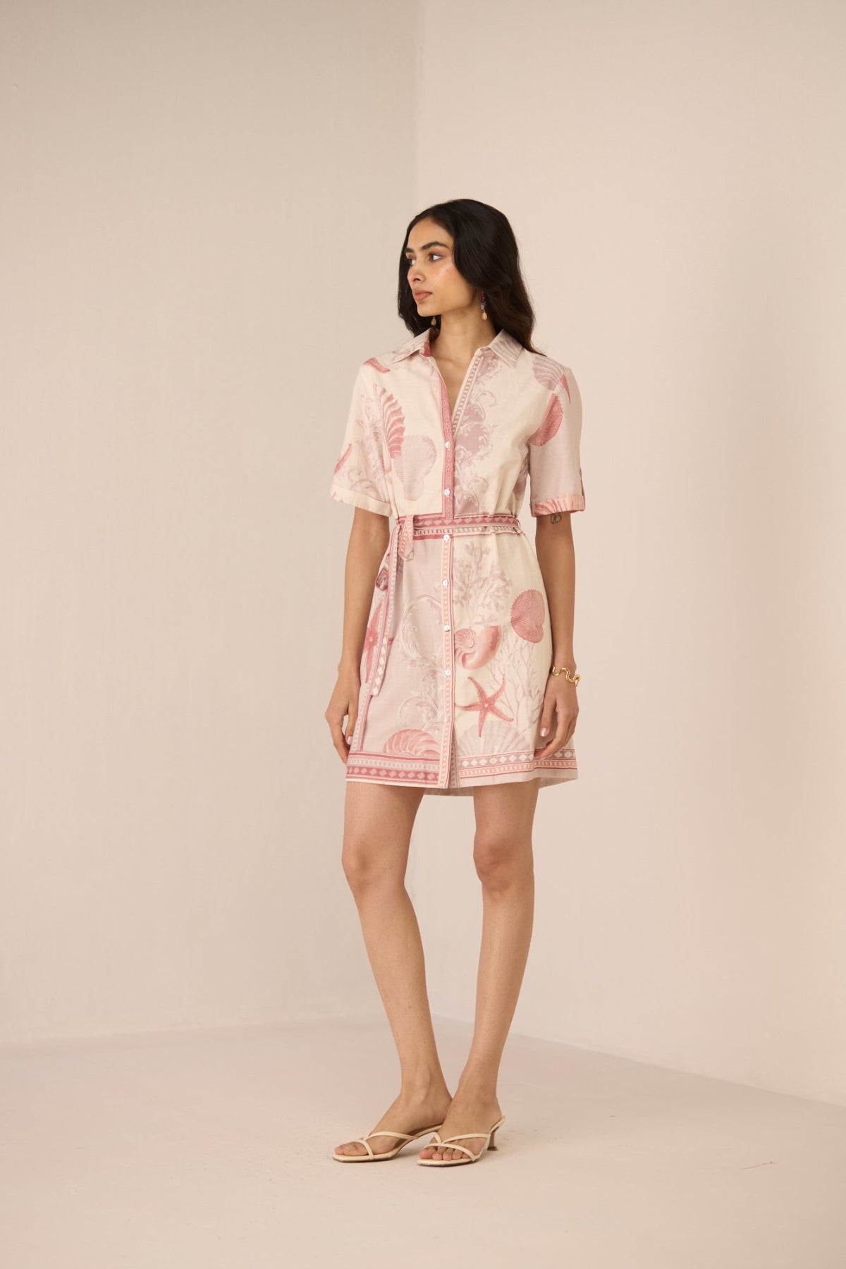 Woman wearing a pink dress with shell pattern on a beige background Calling June