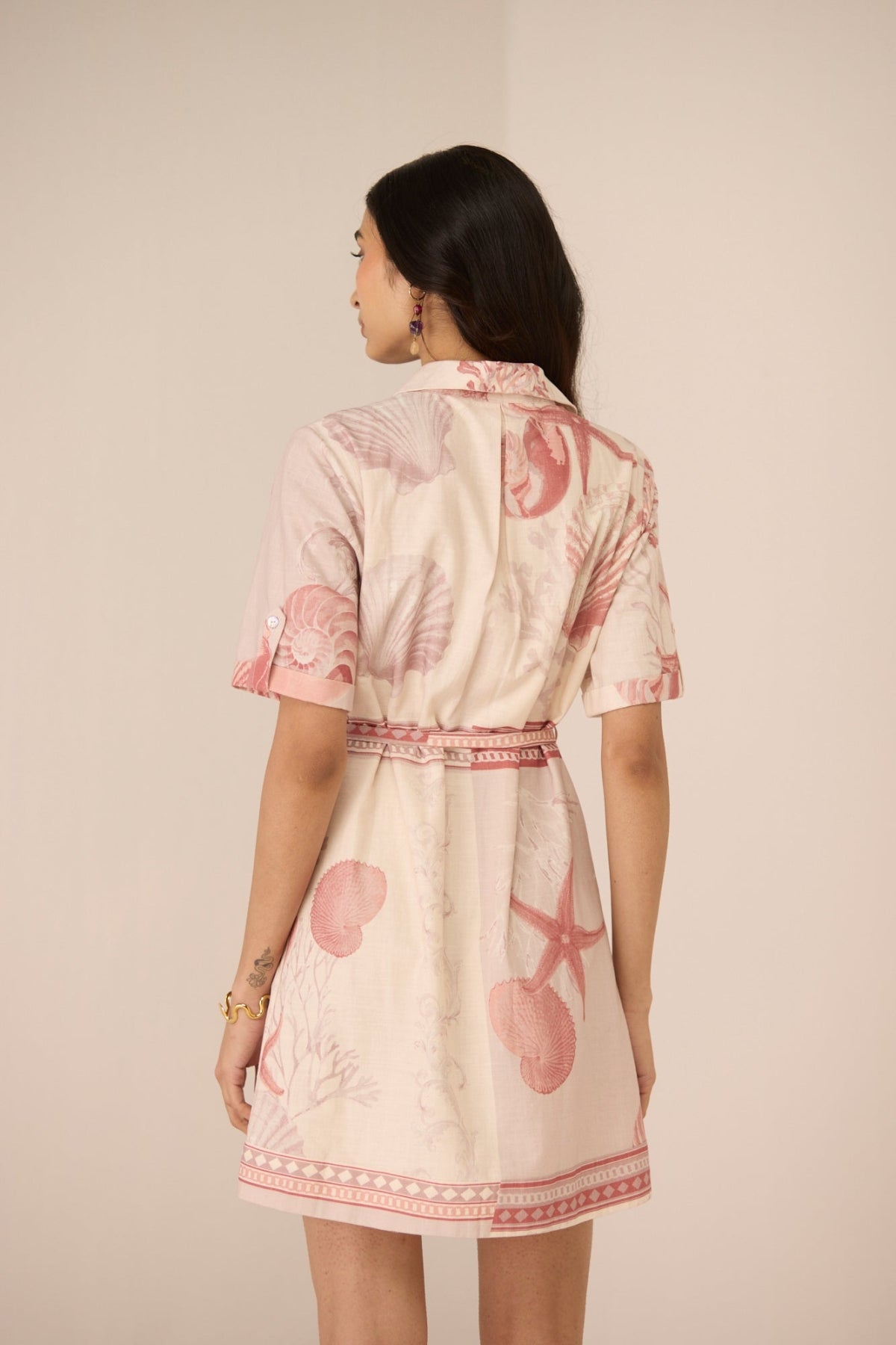 Woman wearing a light-colored dress with pink floral patterns on a plain background Calling June