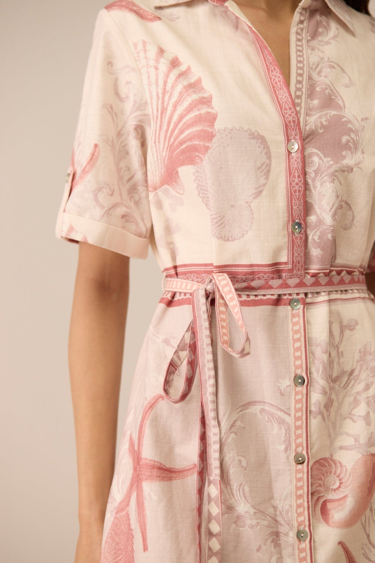 Close-up of a pink and white patterned dress with a belt on a neutral background Calling June