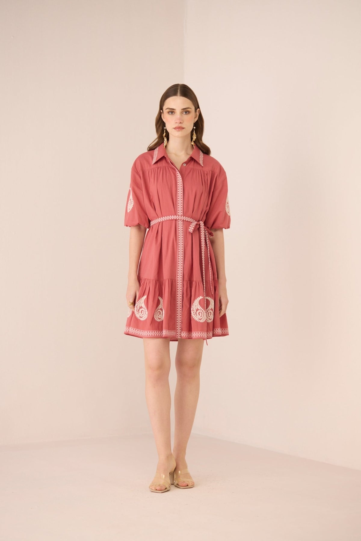 Woman wearing a pink dress with white embroidery on a beige background Calling June