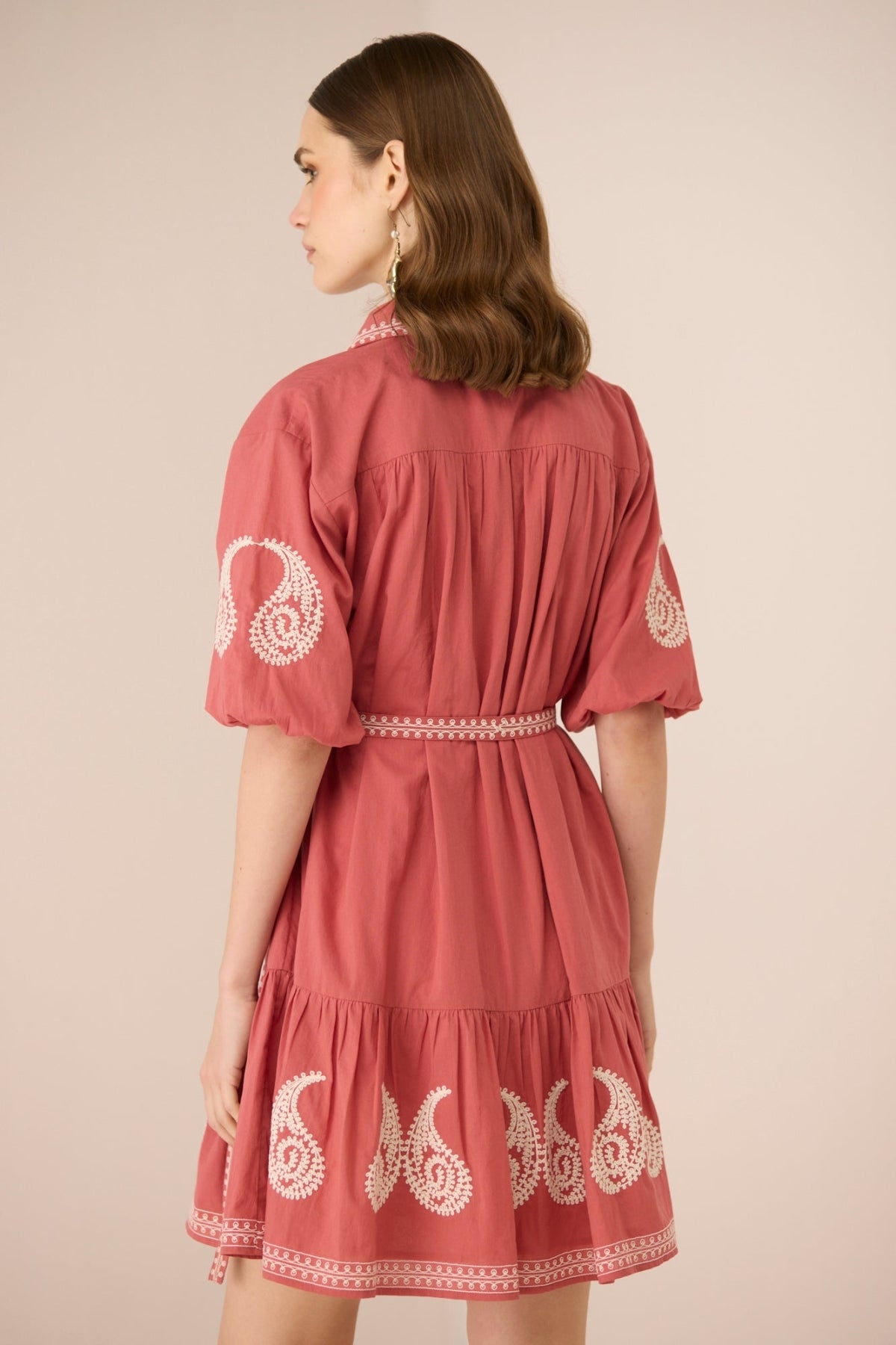 Woman wearing a red dress with white embroidery on a beige background Calling June