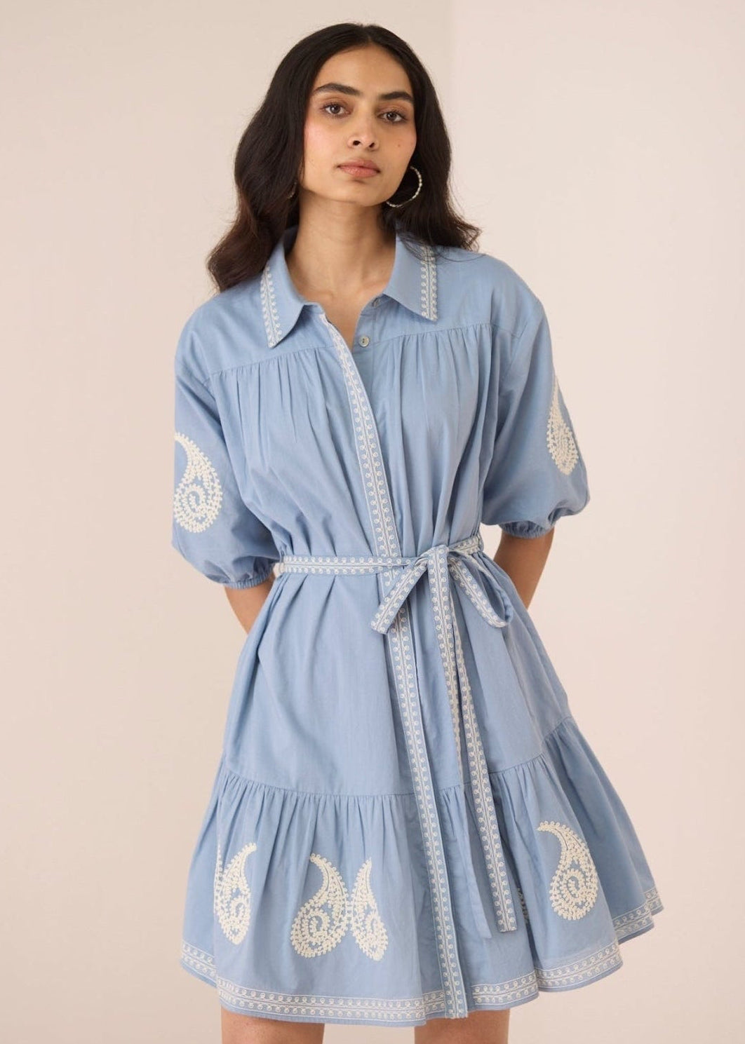 Woman wearing a blue dress with white embroidery on a beige background Calling June