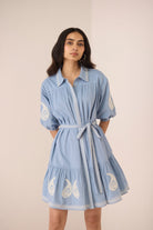 Woman wearing a blue dress with white embroidery on a beige background Calling June