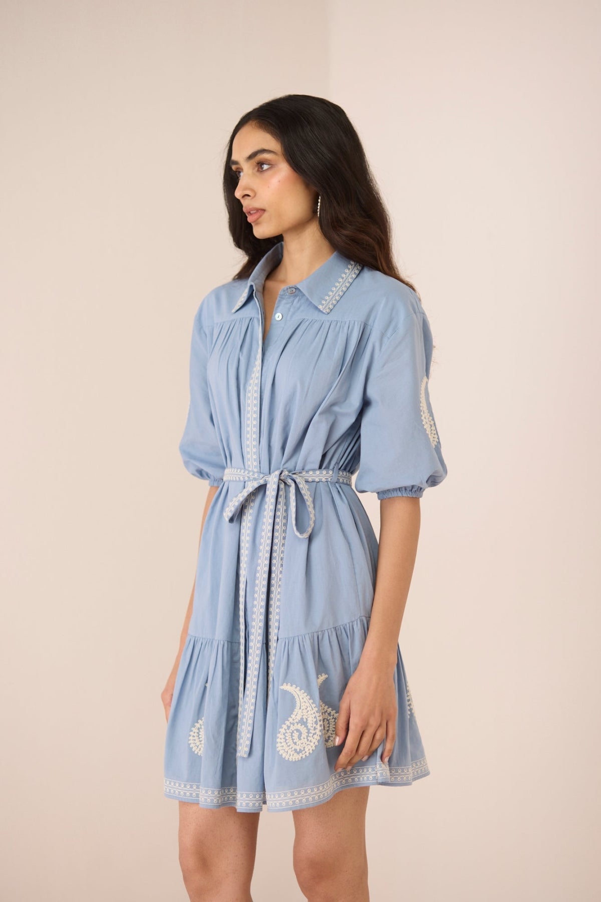 Woman wearing a light blue dress with white embroidery on a beige background Calling June