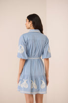 Woman wearing a blue dress with white embroidery on a beige background Calling June