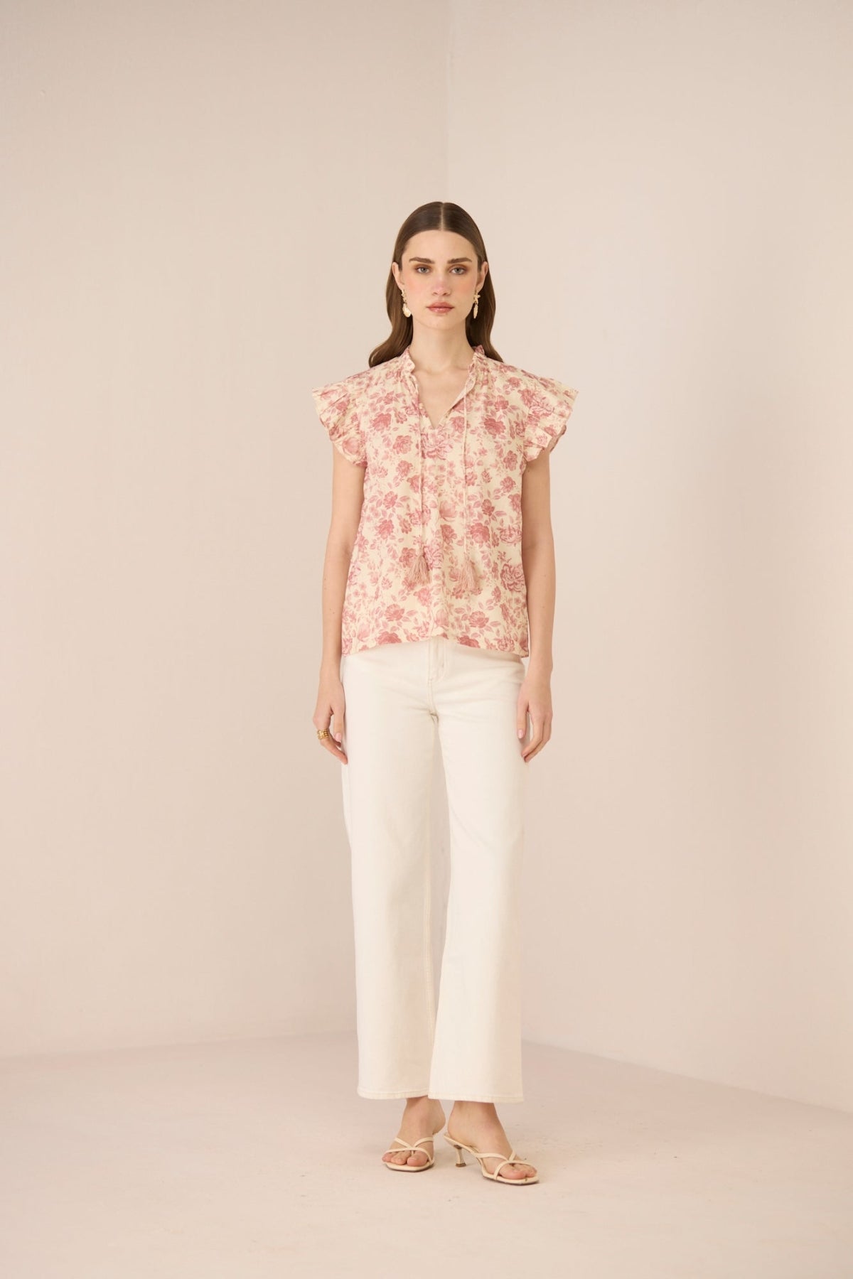Woman wearing a floral blouse and white pants on a beige background Calling June