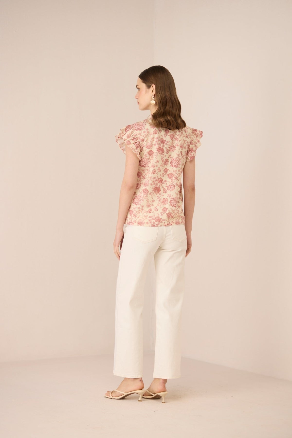 Woman wearing a floral top and white pants on a beige background Calling June