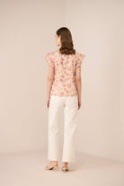 Woman wearing a floral top and white pants on a beige background Calling June