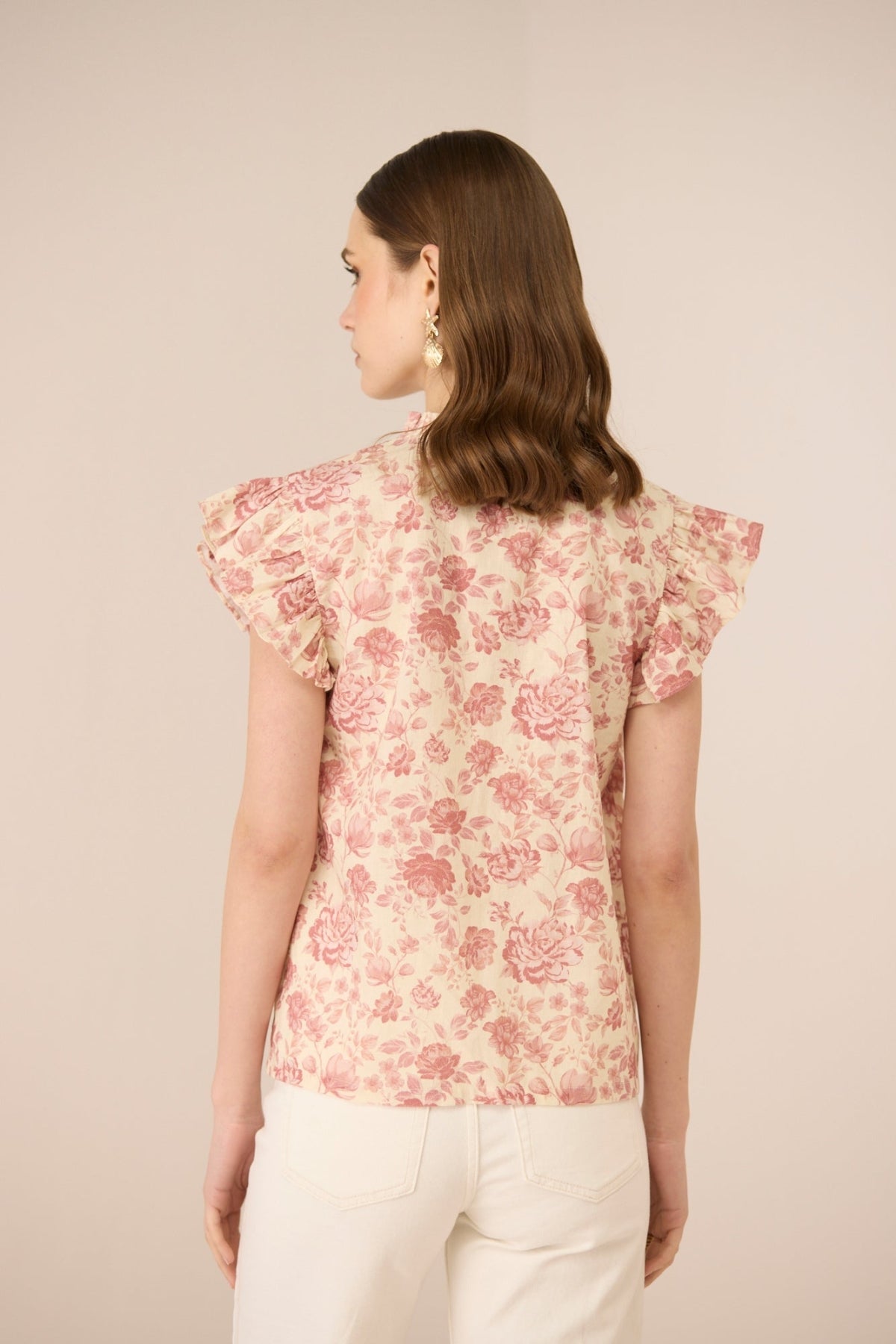 Woman wearing a floral blouse with ruffled sleeves on a beige background Calling June