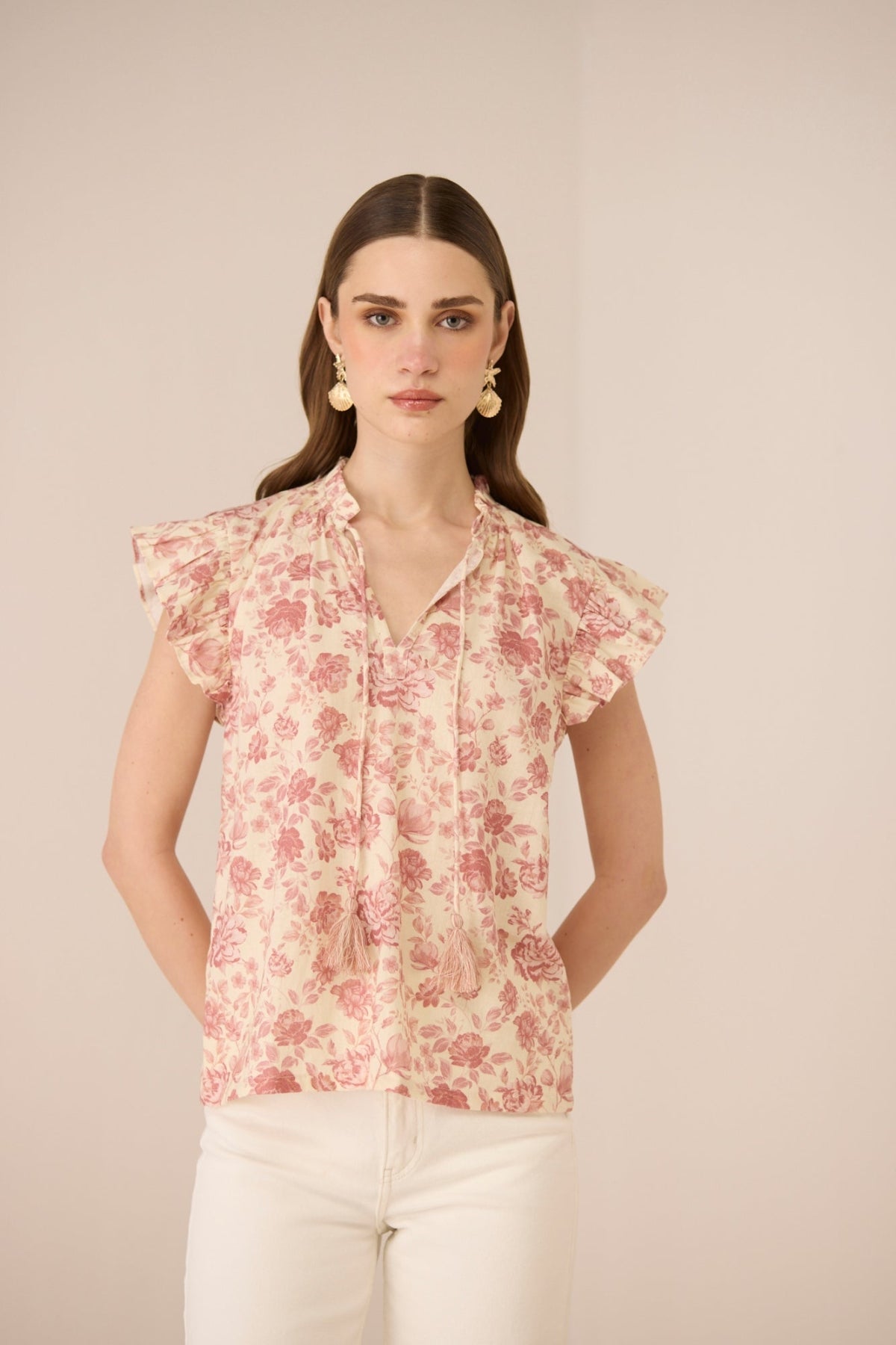 Woman wearing a floral blouse with ruffled sleeves against a beige background Calling June