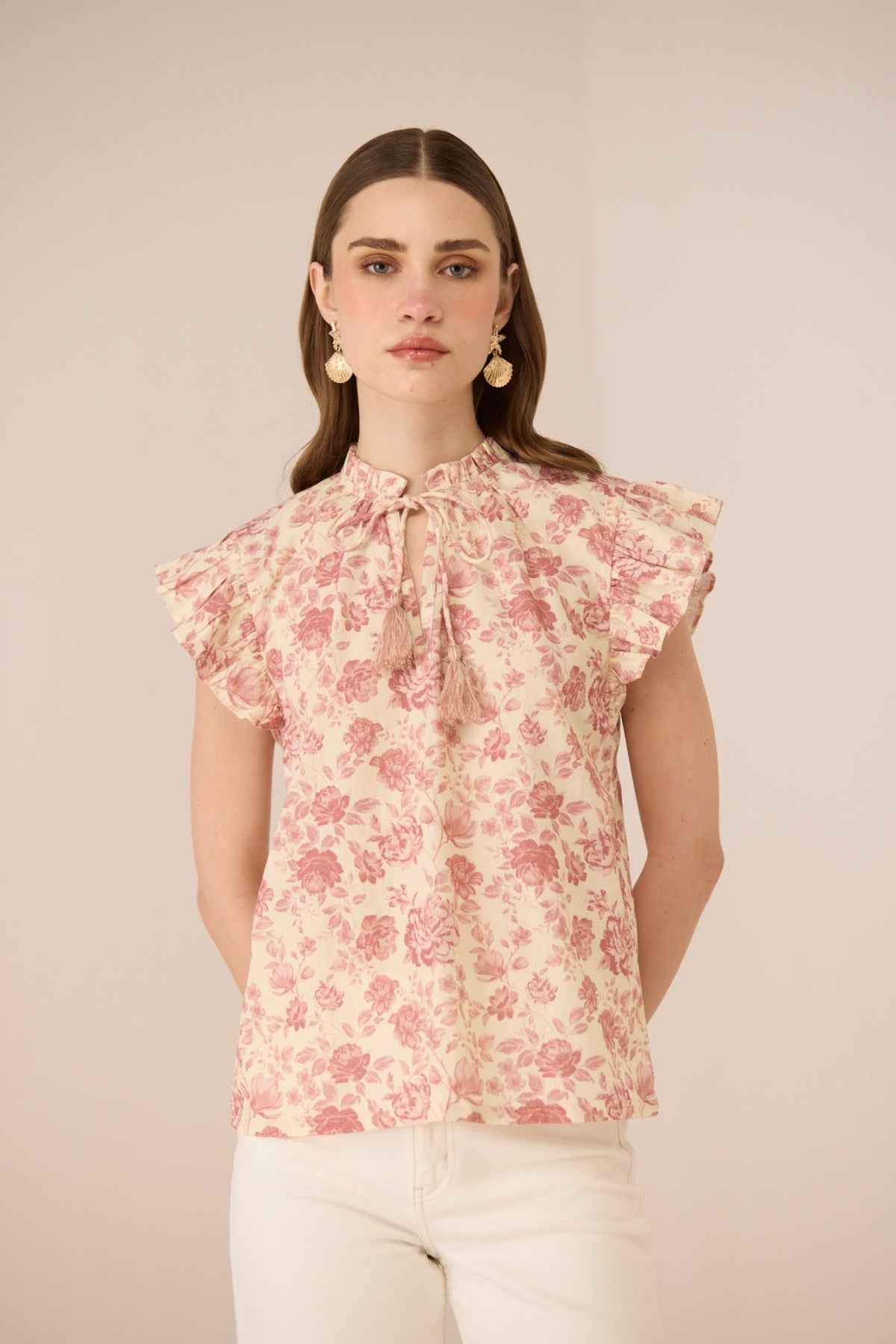 Woman wearing a floral blouse with ruffled sleeves against a beige background Calling June