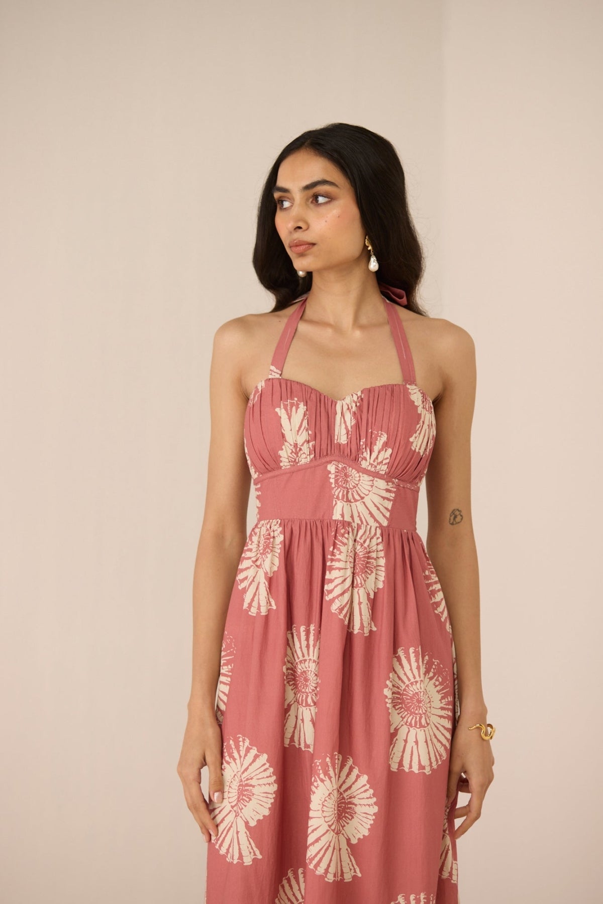 Woman wearing a pink dress with white floral patterns against a beige background Calling June