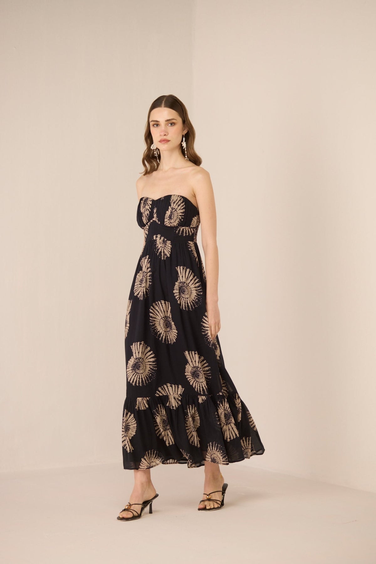 Woman wearing a strapless black dress with gold sunflower pattern on a beige background Calling June