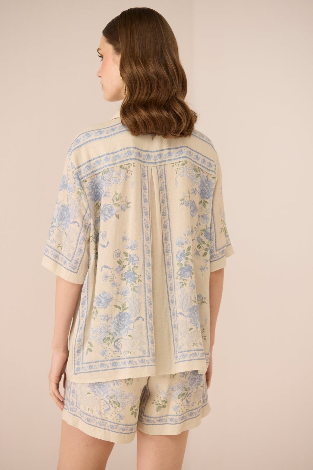 Woman wearing a beige outfit with floral patterns on a plain background Calling June