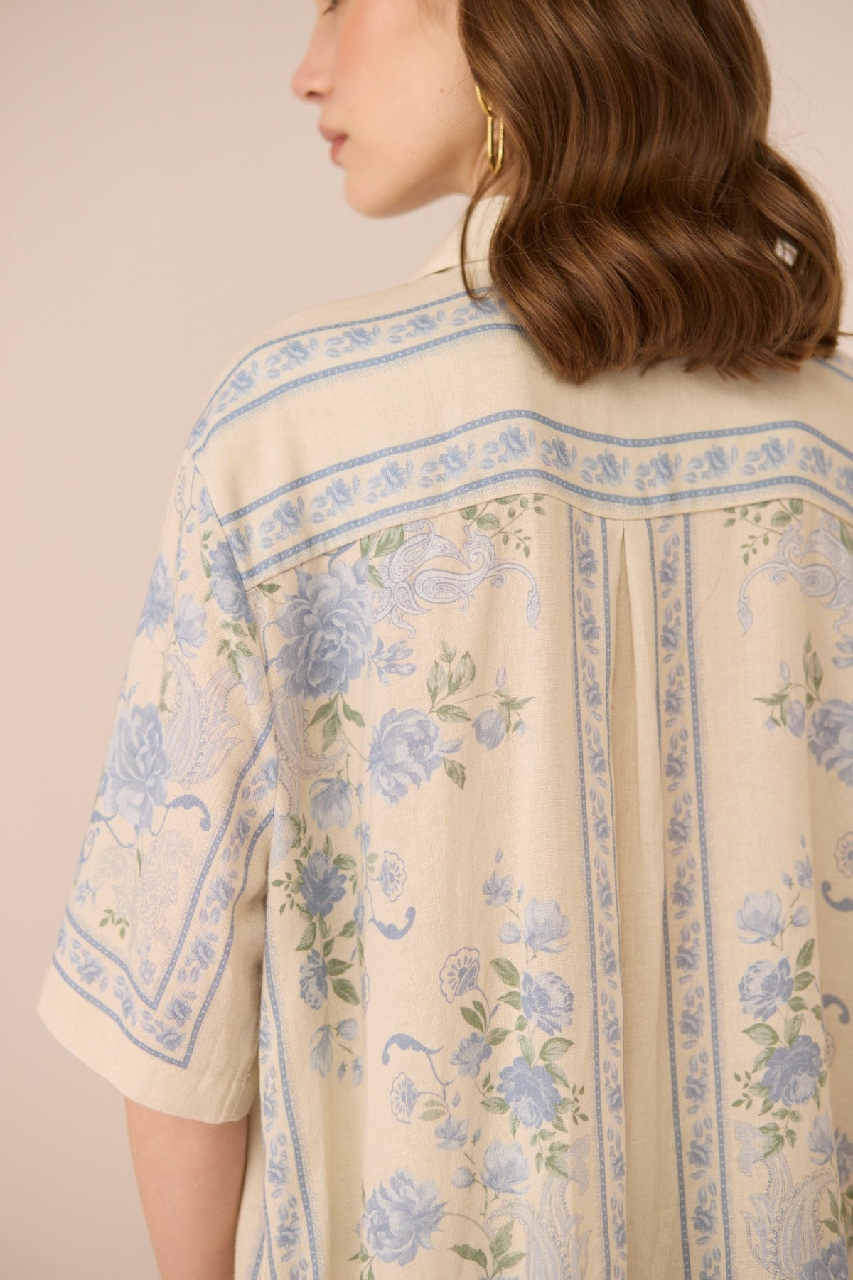 Beige shirt with blue floral patterns worn by a person against a beige background Calling June