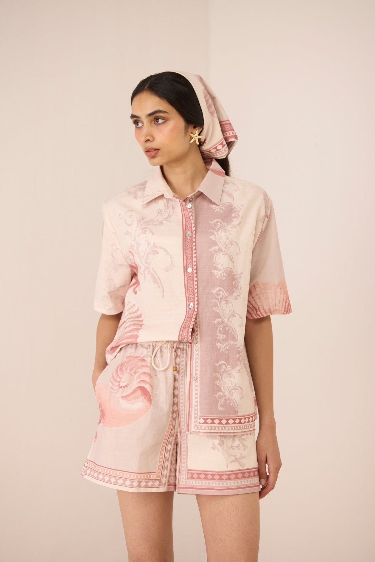 Woman wearing a pink and white patterned outfit with a matching headscarf against a beige background Calling June