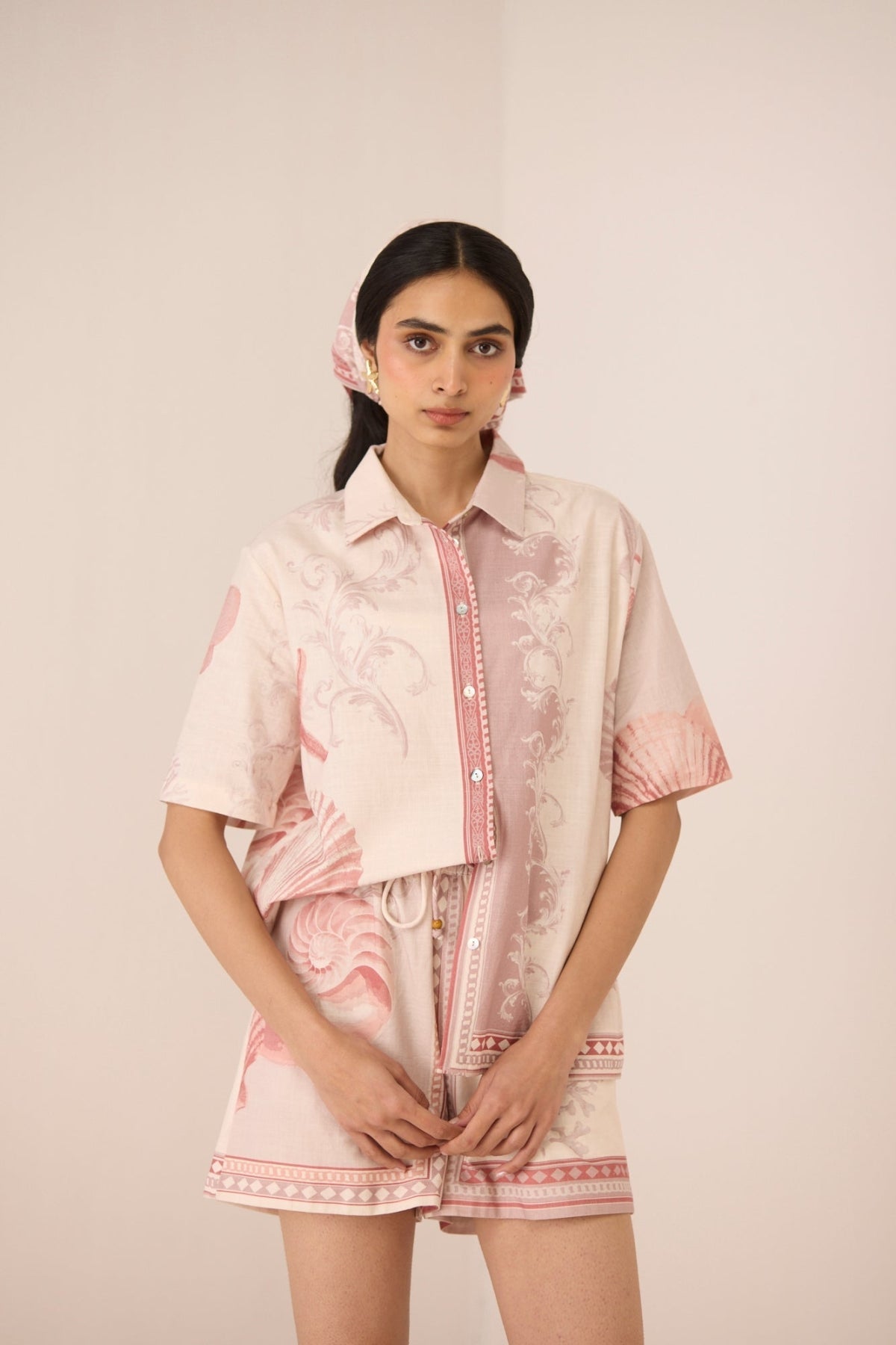 Woman wearing a pink and white outfit with a matching jacket and shorts on a plain background Calling June