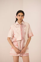 Woman wearing a pink and white outfit with a matching jacket and shorts on a plain background Calling June