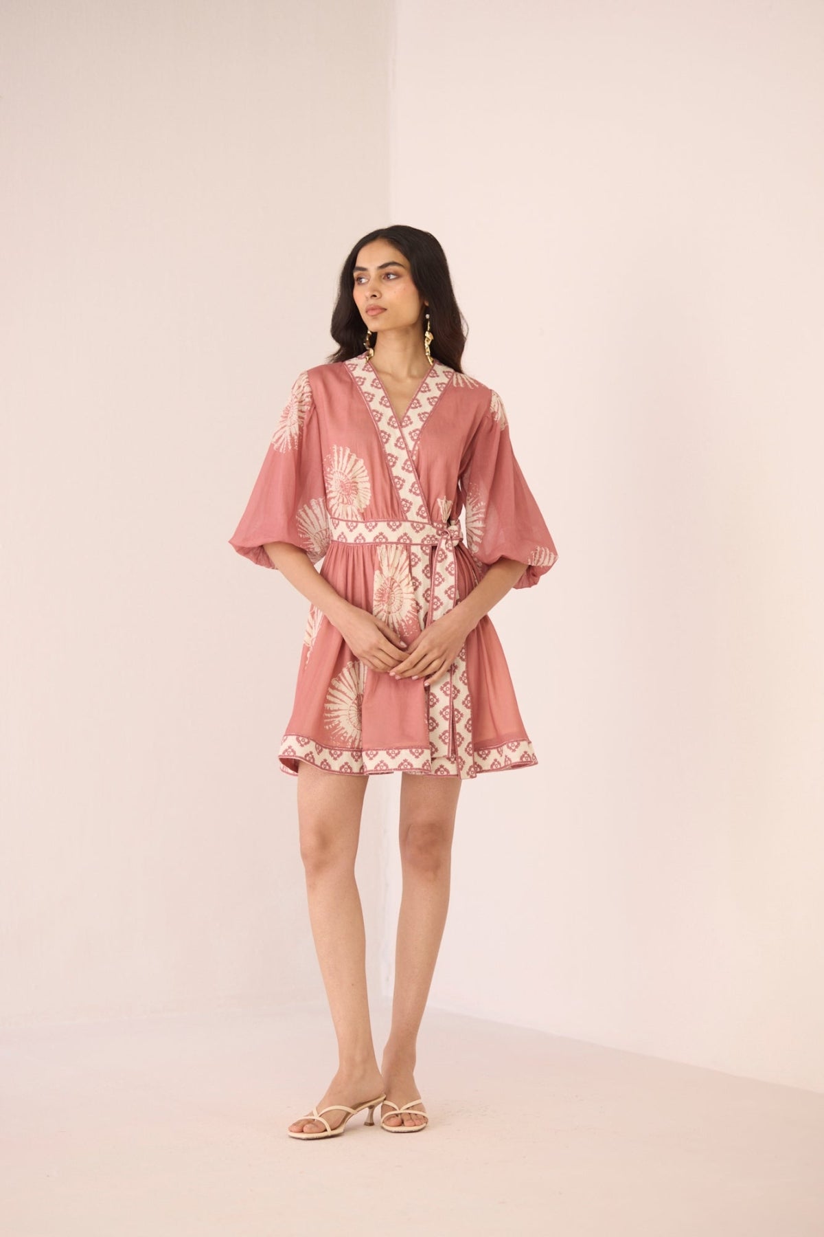 Woman wearing a pink dress with white lace details on a plain background Calling June