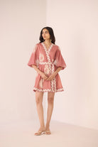 Woman wearing a pink dress with white lace details on a plain background Calling June