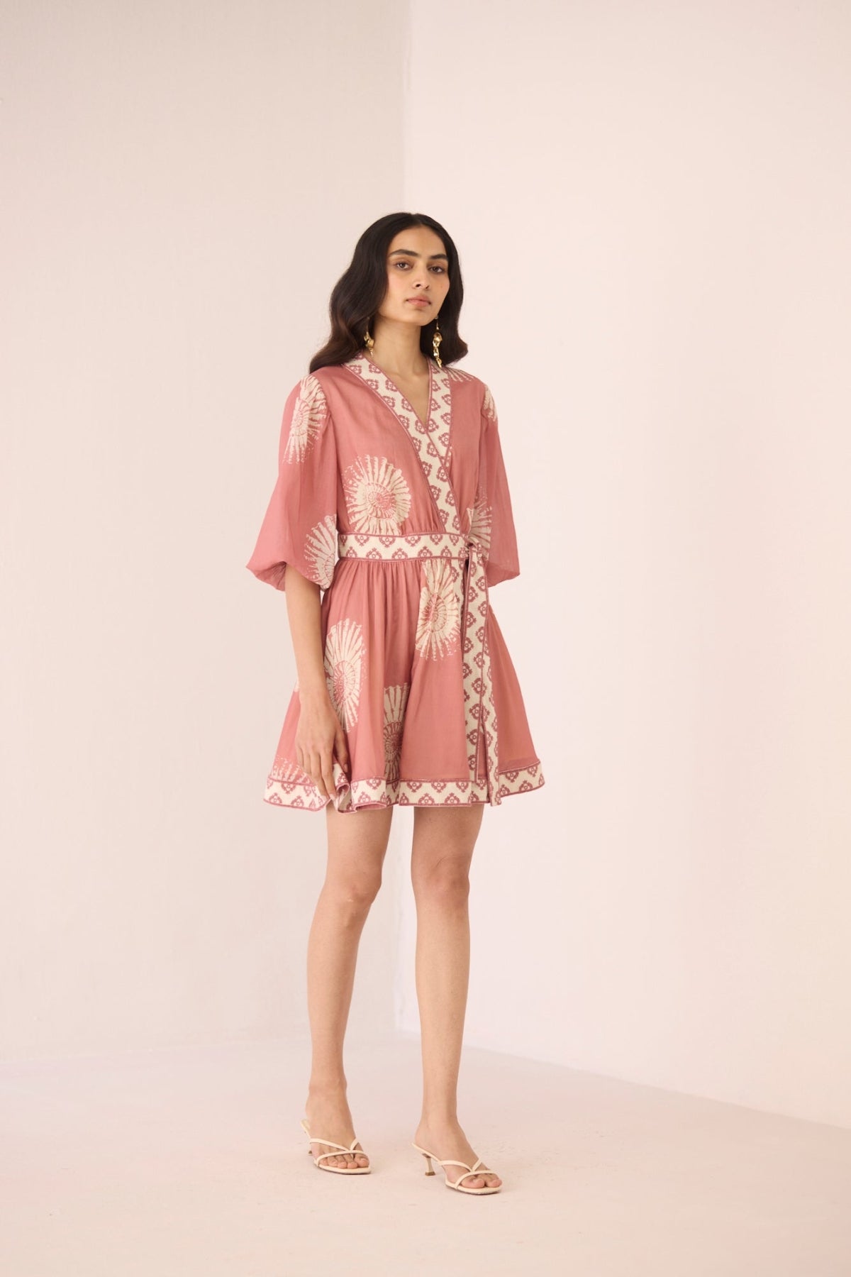 Woman wearing a pink dress with white patterns on a plain background Calling June