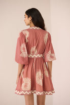 Woman wearing a pink dress with white patterns on a plain background Calling June