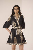 Woman wearing a black dress with gold patterns on a plain background Calling June