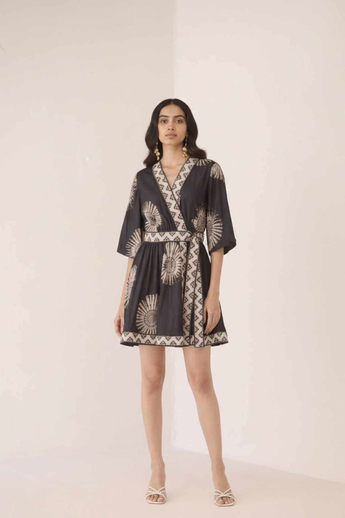 Woman wearing a black and gold patterned dress on a plain background Calling June