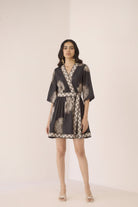 Woman wearing a black and gold patterned dress on a plain background Calling June