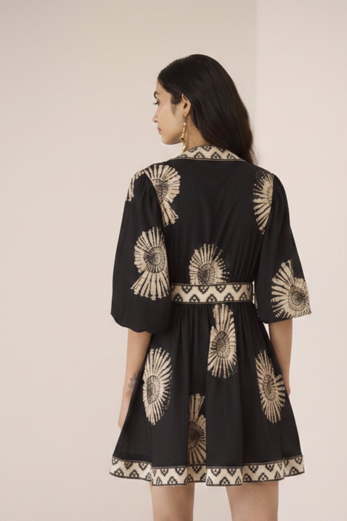 Woman wearing a black dress with gold patterns on a beige background Calling June