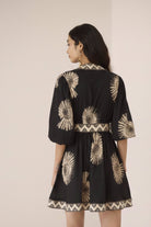 Woman wearing a black dress with gold patterns on a beige background Calling June