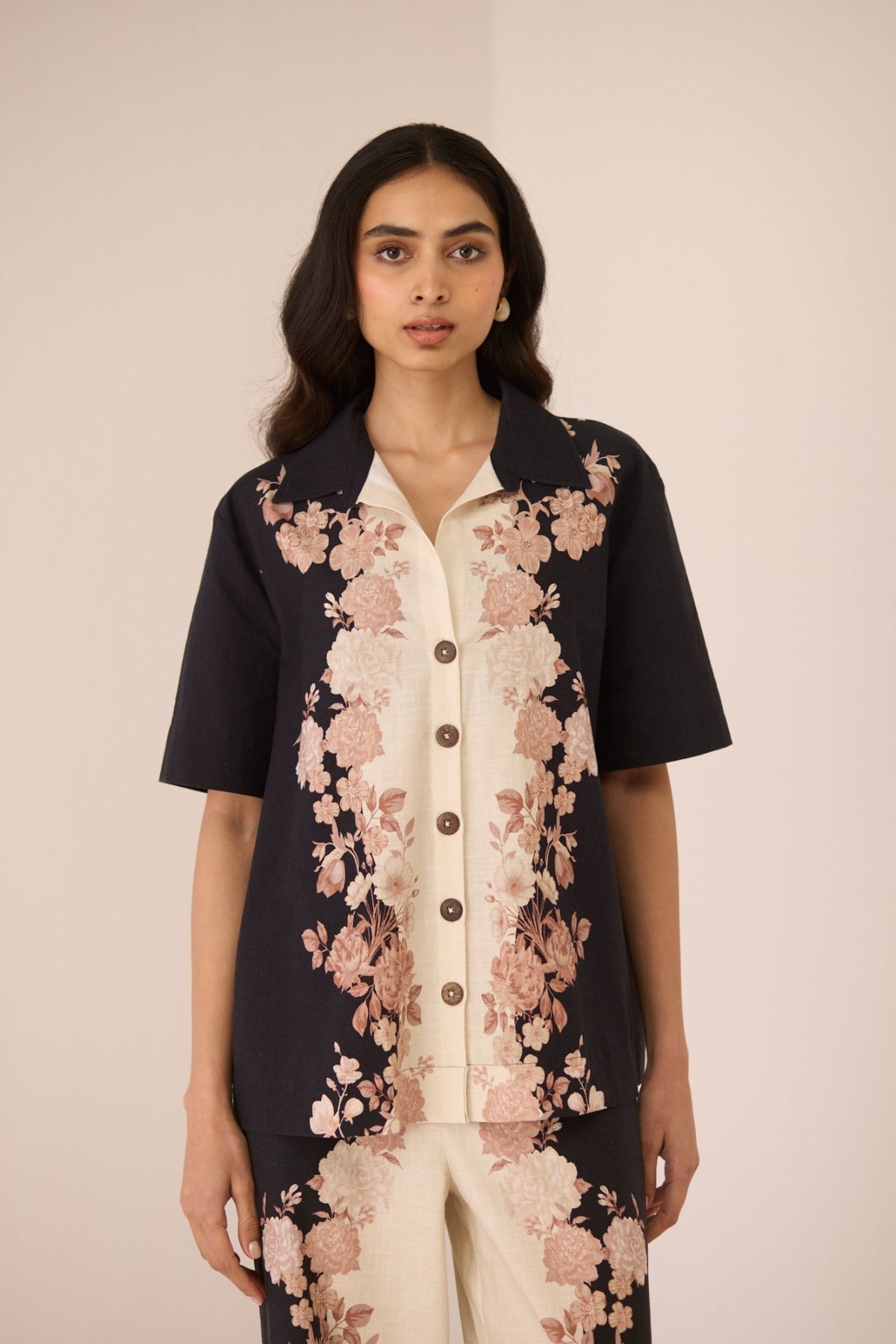 Woman wearing a black floral jacket over a cream shirt with matching pants on a beige background Calling June