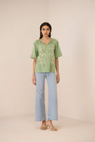 Woman wearing a green embroidered top and light blue jeans on a beige background Calling June